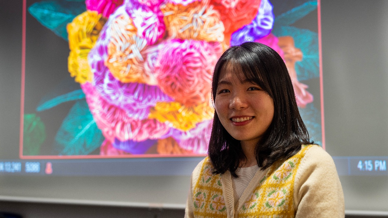 Yeonjin Baek poses in front of a display of "Flower Power," which won the grand prize in JEOL'S 2023 SEM Image Contest.