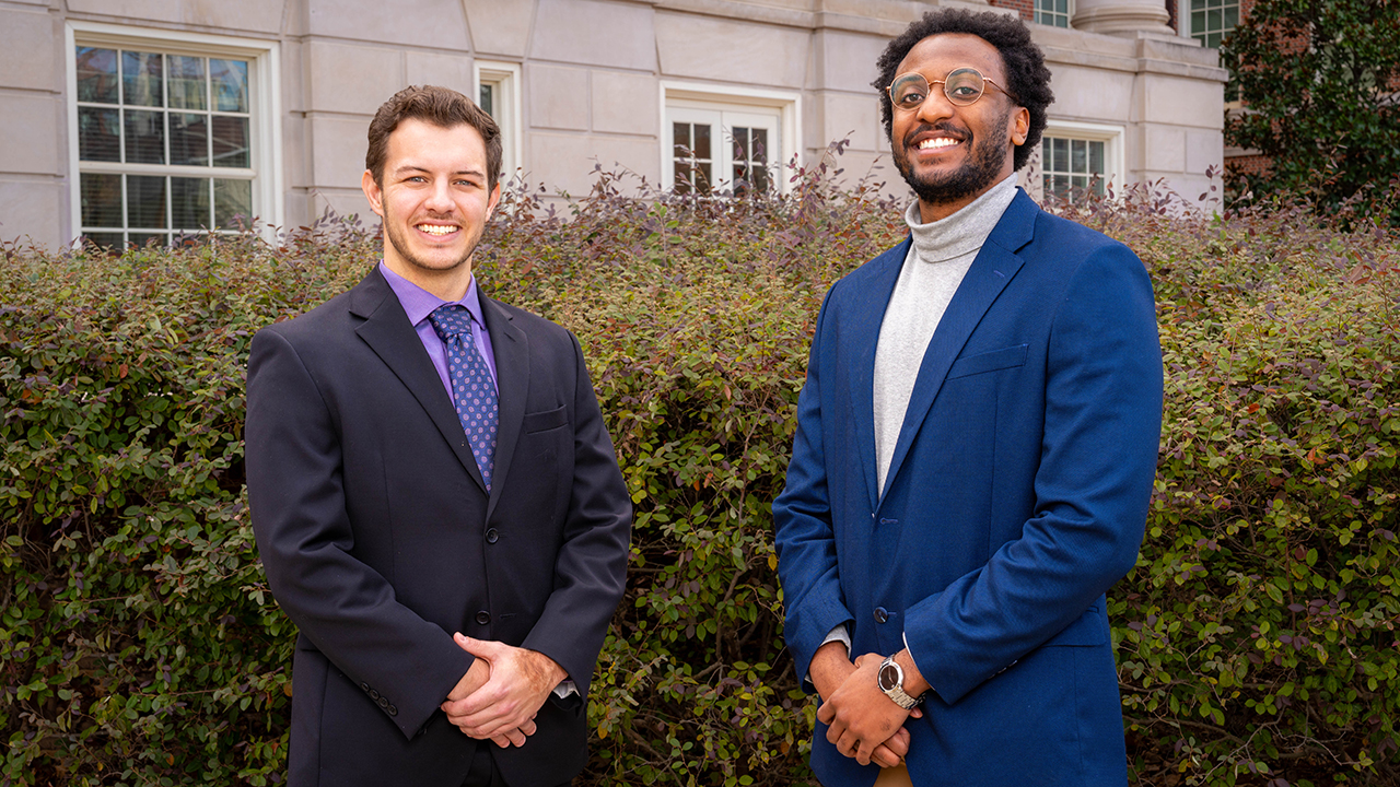 two men pose for a photo outside