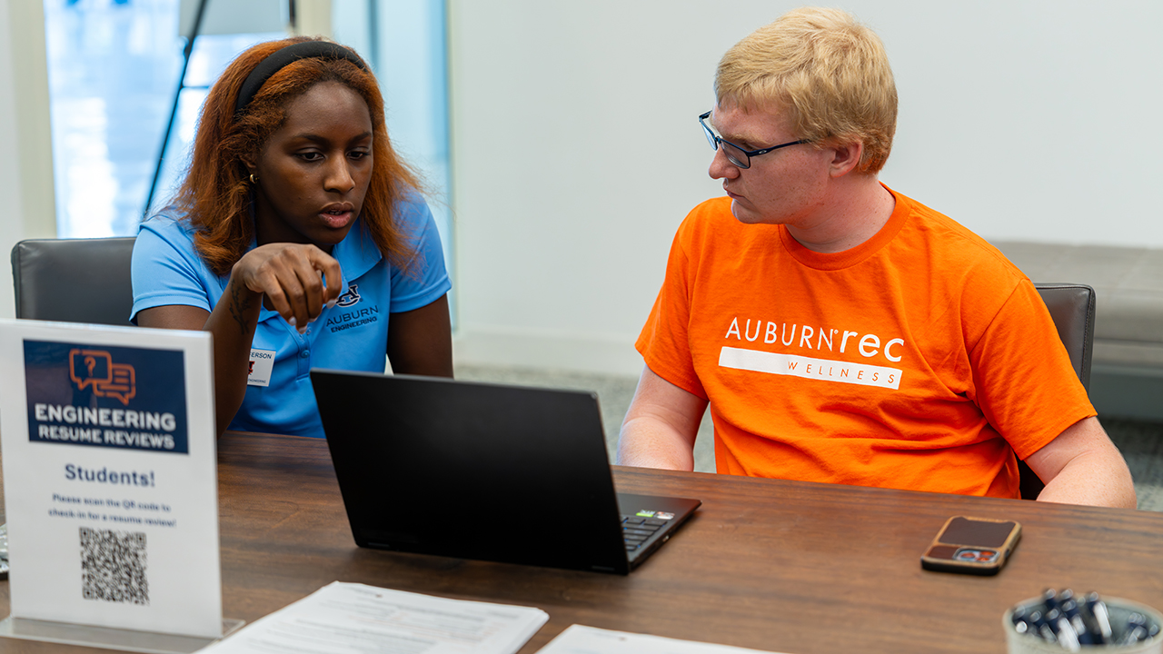 CDCR peer mentor sitting with a student and discussing a résumé on a laptop during an Auburn Engineering résumé review session.