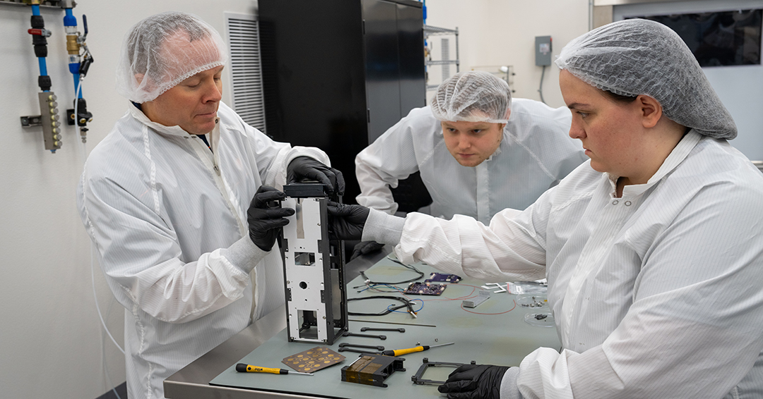 From left, Mark Adams, the Godbold Professor in electrical and computer engineering, TES research engineer Ben Colvett and research engineer Elizabeth McMeen build the framework for a satellite.