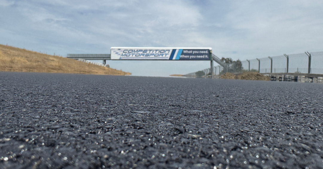 Close-up view of the newly paved asphalt surface at Thunderhill Raceway Park’s East Course, looking down the racetrack toward an overhead bridge.