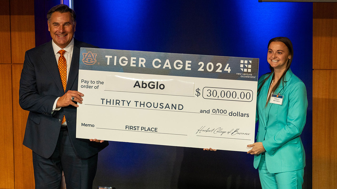 AbGlo co-founder and engineering management online graduate student Holli Michaels, right, accepts the first place check from Tiger Cage emcee Mark Forchette, who earned a degree in marketing from Auburn in 1981.