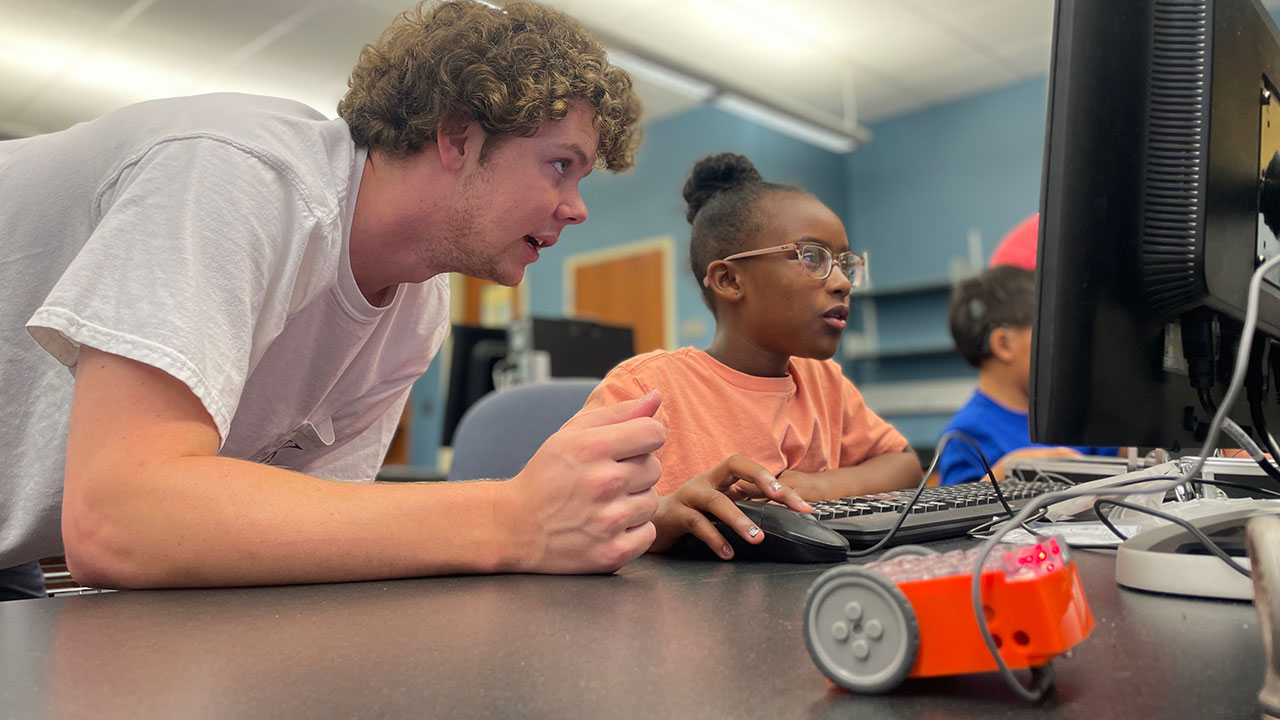 Third grader Zoe Akins receives instruction from computer science and software engineering student Travis Thompson.