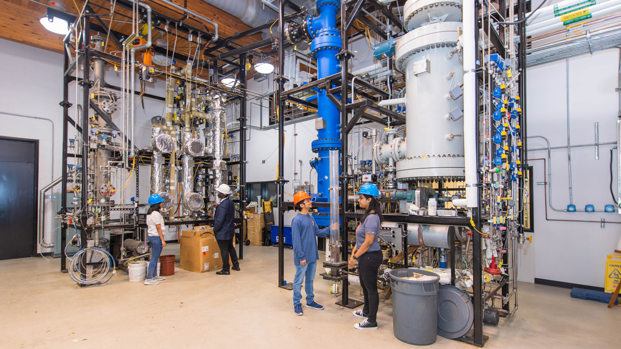 Students in the Bioenergy and Bioproducts Center standing in front of a bubbling-fluidized bed gasification system for producing hydrogen and other gaseous fuels.