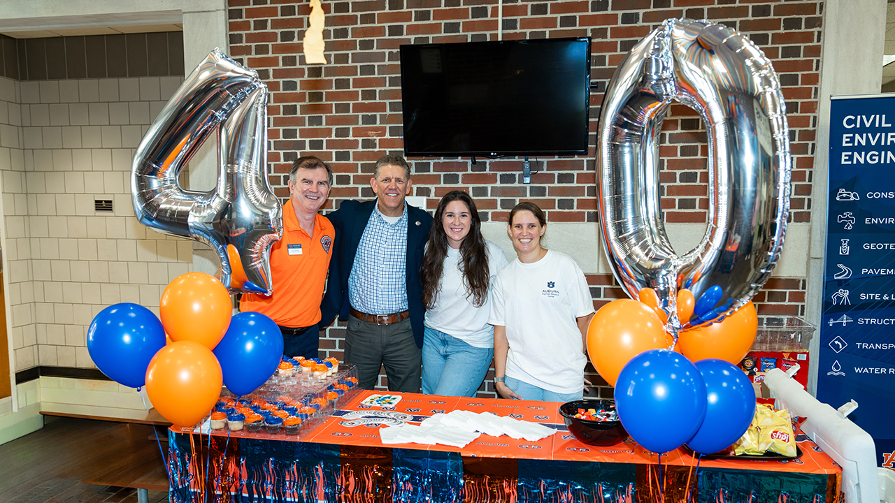 Anton Schindler, David Timm, Corie McConnell and Katie Fall stand behind an orange table with silver balloons with 40 spelled out as well as orange and blue balloons