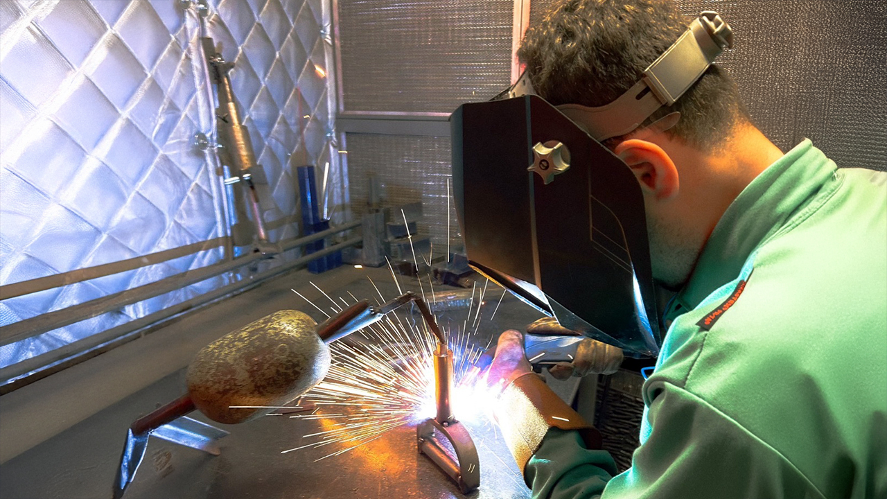 A student with a welding mask working on metal bar.