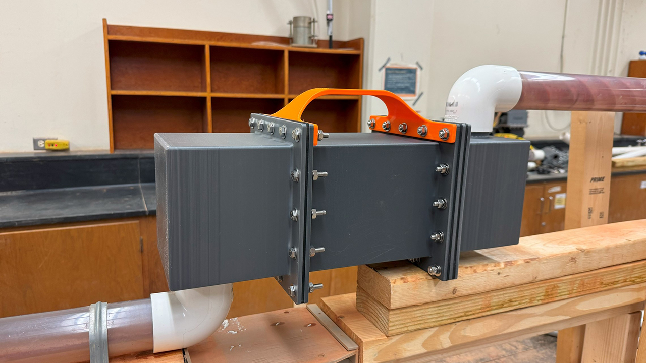 a black metal box with a orange handle sits on a piece of wood