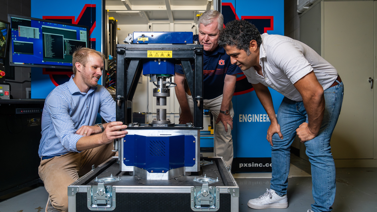 three men looking at blue x-ray machine.