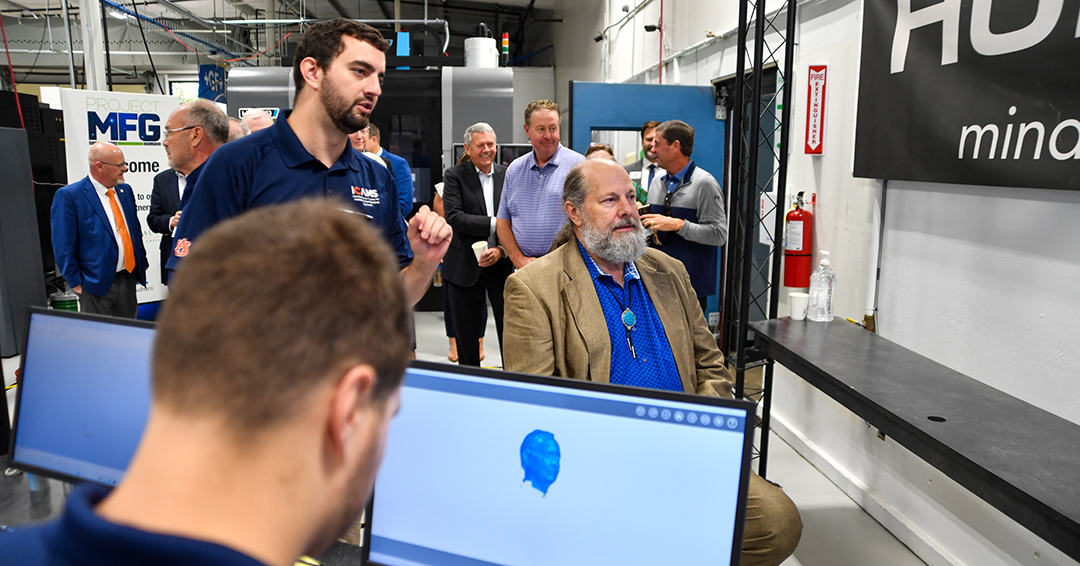 Visitors tour an advanced manufacturing lab as a staff member demonstrates equipment and digital scanning technology.