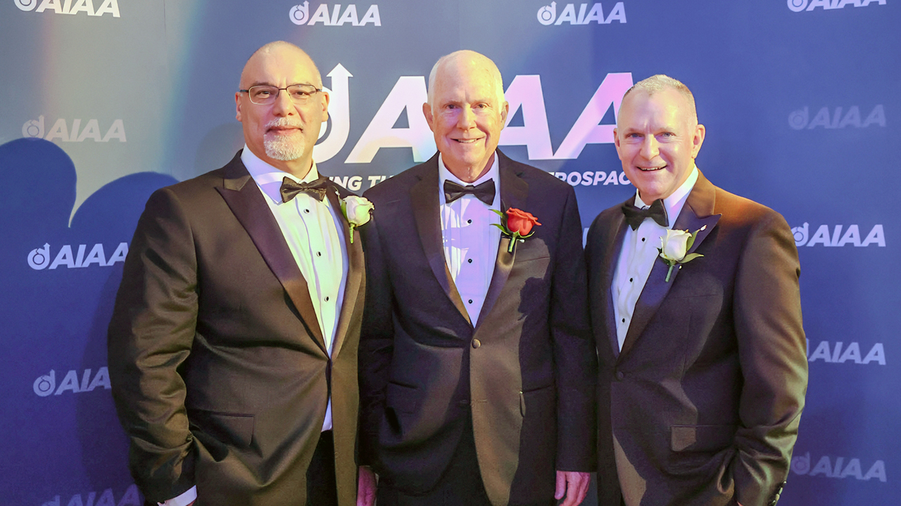 Three men pose for a photo in black suits.