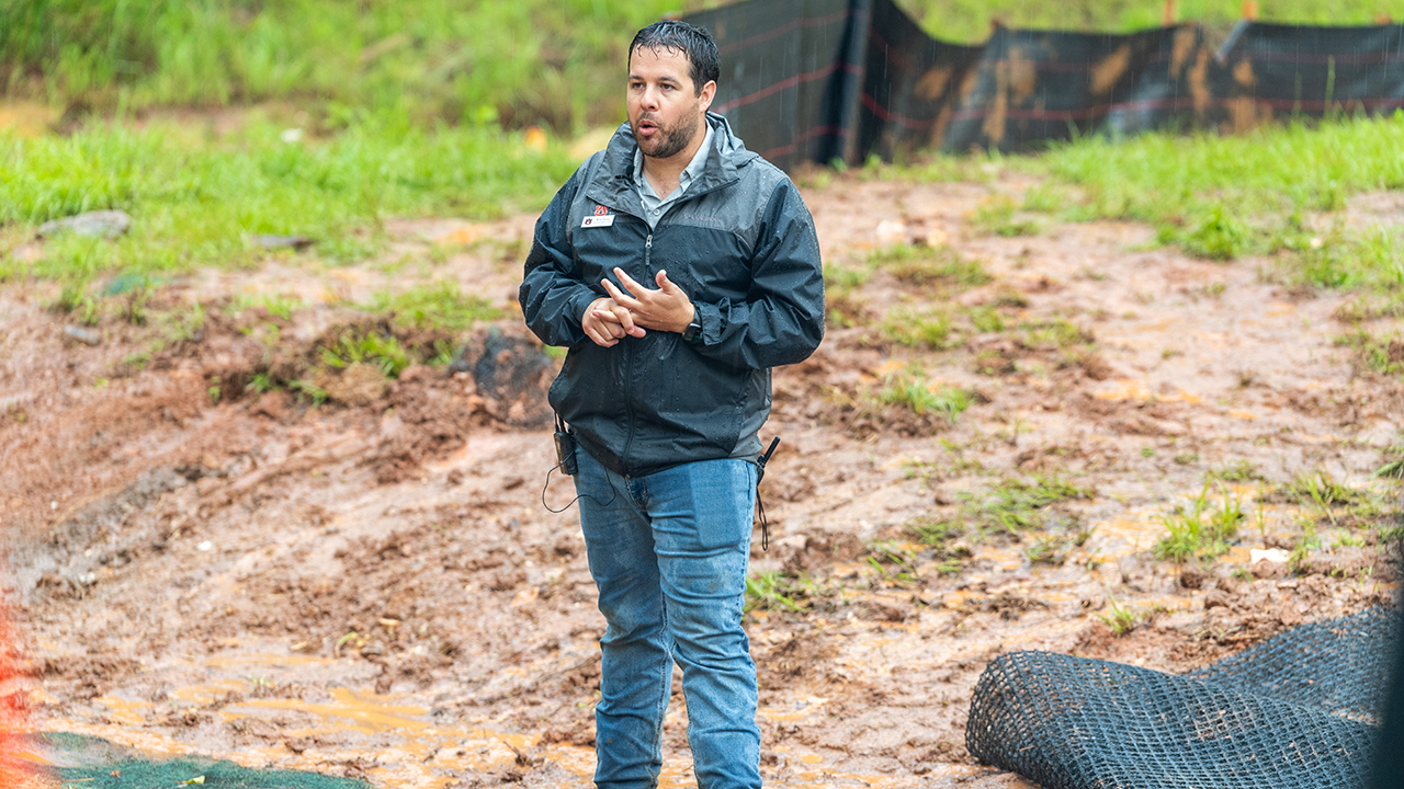 A man in a black raincoat talks while it’s raining.