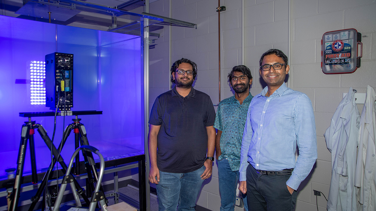 three people looking at a box glowing purple in a lab.