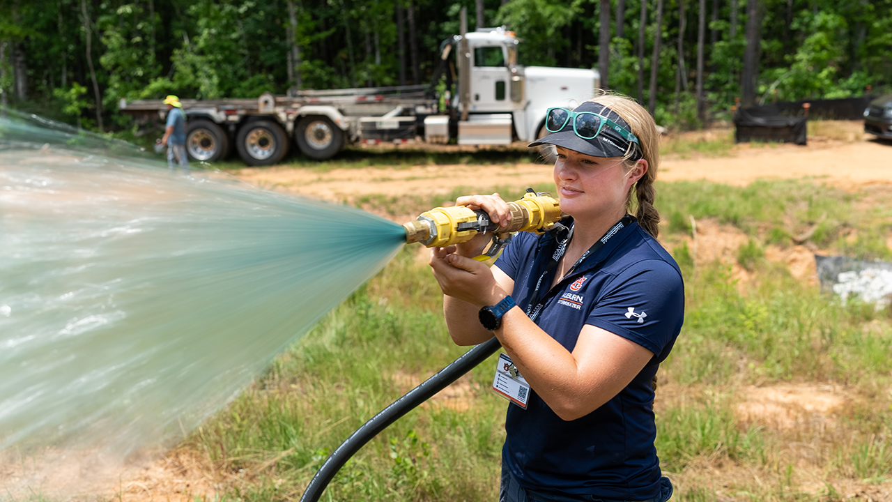 A woman sprays a powerful hose at a erosion and sediment control workshop at the Auburn University Stormwater Research Facility.