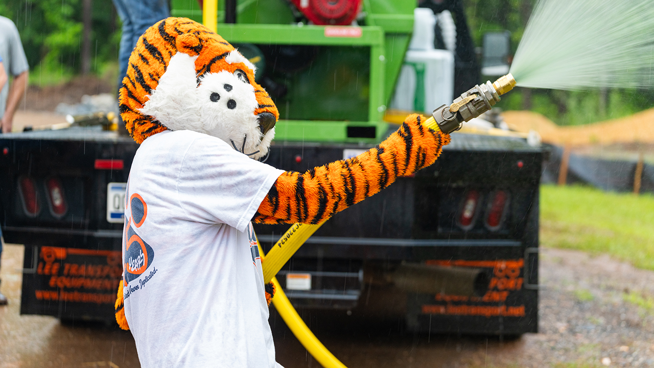 Auburn mascot Aubie sprays hydromulch in the rain to the delight of the field day participants.